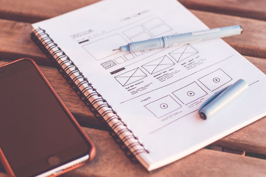A hand-drawn UI wireframe in a notebook next to a phone.